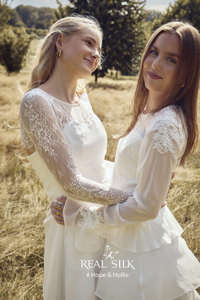 To kvinder i hvide blondekjoler omfavner hinanden udendørs